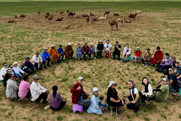 Mongolia meeting with circle of people with Camels in background.