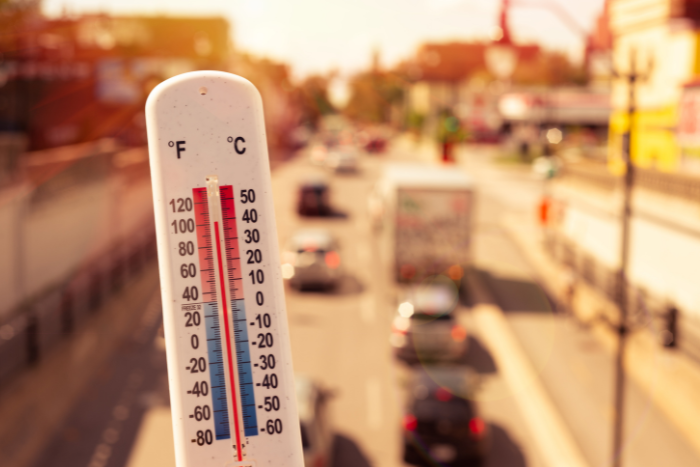 Thermometer showing high temperature with traffic in background